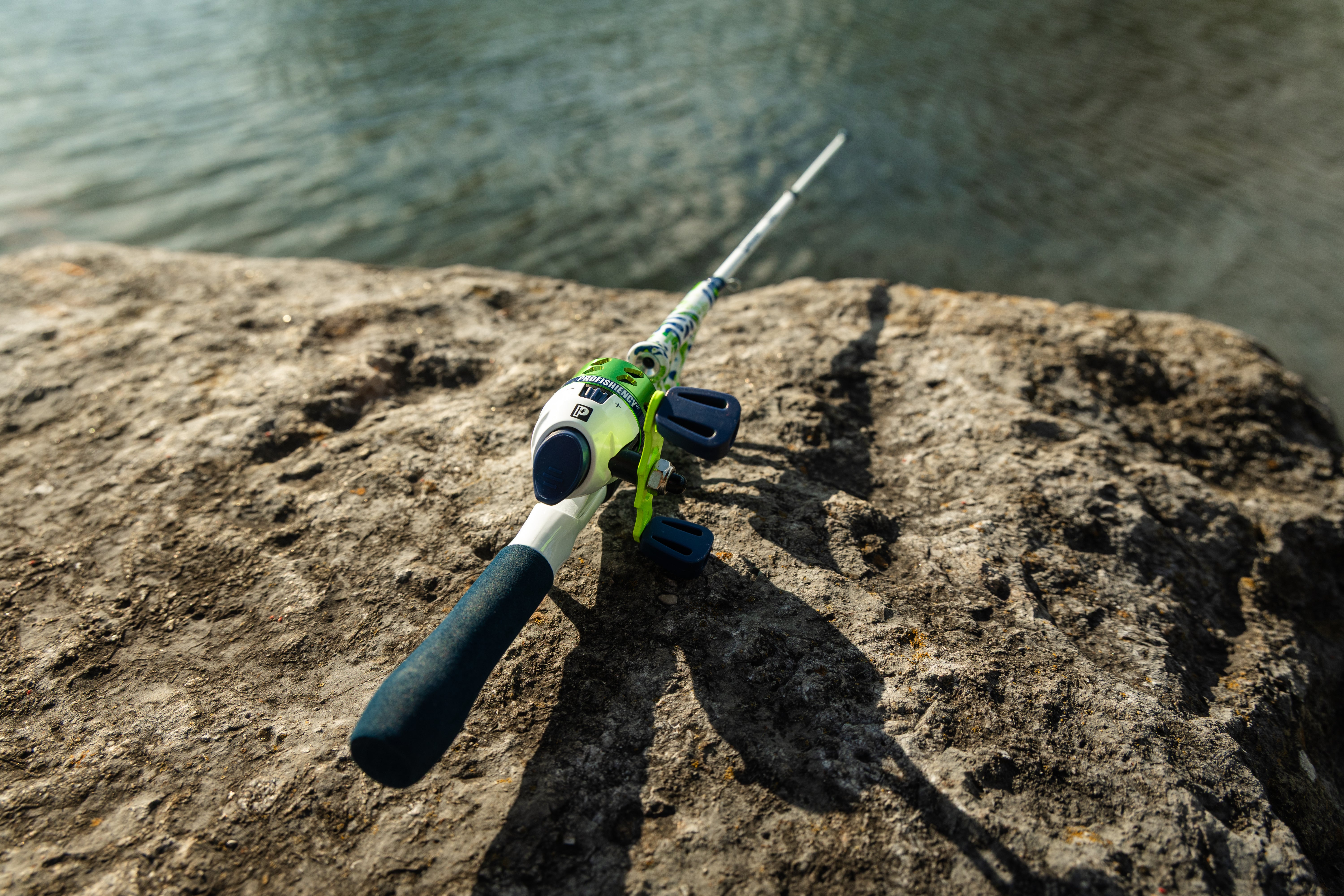 Angled close-up of Green Briyo Tiny Pocket Combo showcasing its green and blue reel beside a rocky shoreline