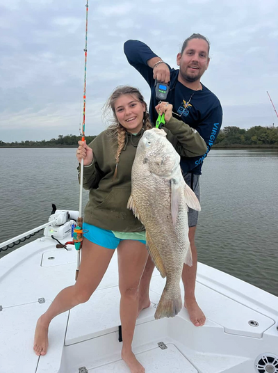 Smiling woman and man on a boat holding a very large fish by its lip