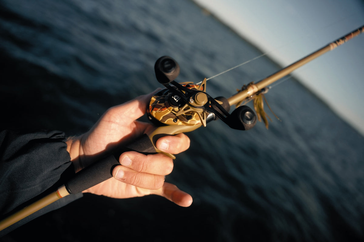 Close-up of Retro Baitcast Reels - Clam Pack showcasing classic-camo design in hand over water