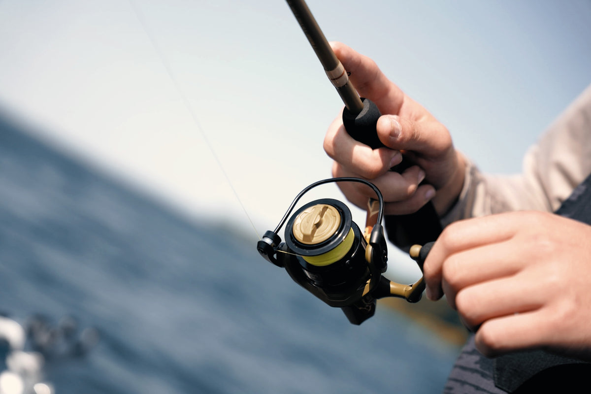Angler reeling a black and gold spinning rod over the water