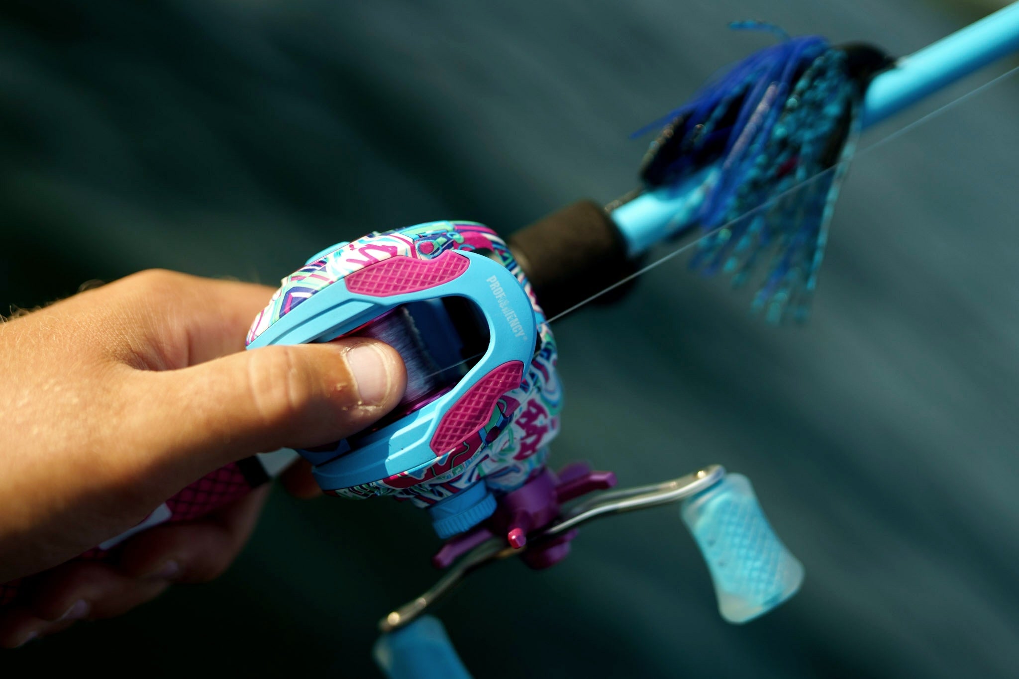 Close-up of Wild Child Baitcast Combo showcasing its colorful patterned reel and blue rod in use against a dark background