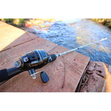 Close-up of Profishiency Strata Dock Combo rod and baitcasting reel showcasing reel handle and foam grip with wooden dock and stream background