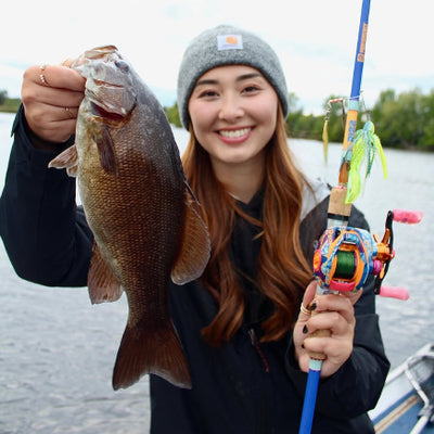 Smiling woman on a boat holding a large bass and a colorful baitcasting rod with a lure